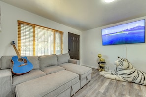 Ein Wohnzimmer mit einem Ecksofa, einer Gitarre, einer Tigerstatue und einem Fernseher an der Wand.