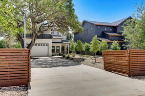 Een modern huis met twee verdiepingen, een overdekte patio, een oprit en een houten omheining.