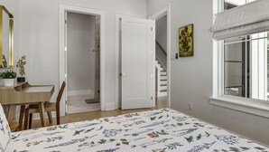 Ett sovrum med en säng, ett skrivbord, en stol, en dörr, en trappa och ett fönster.