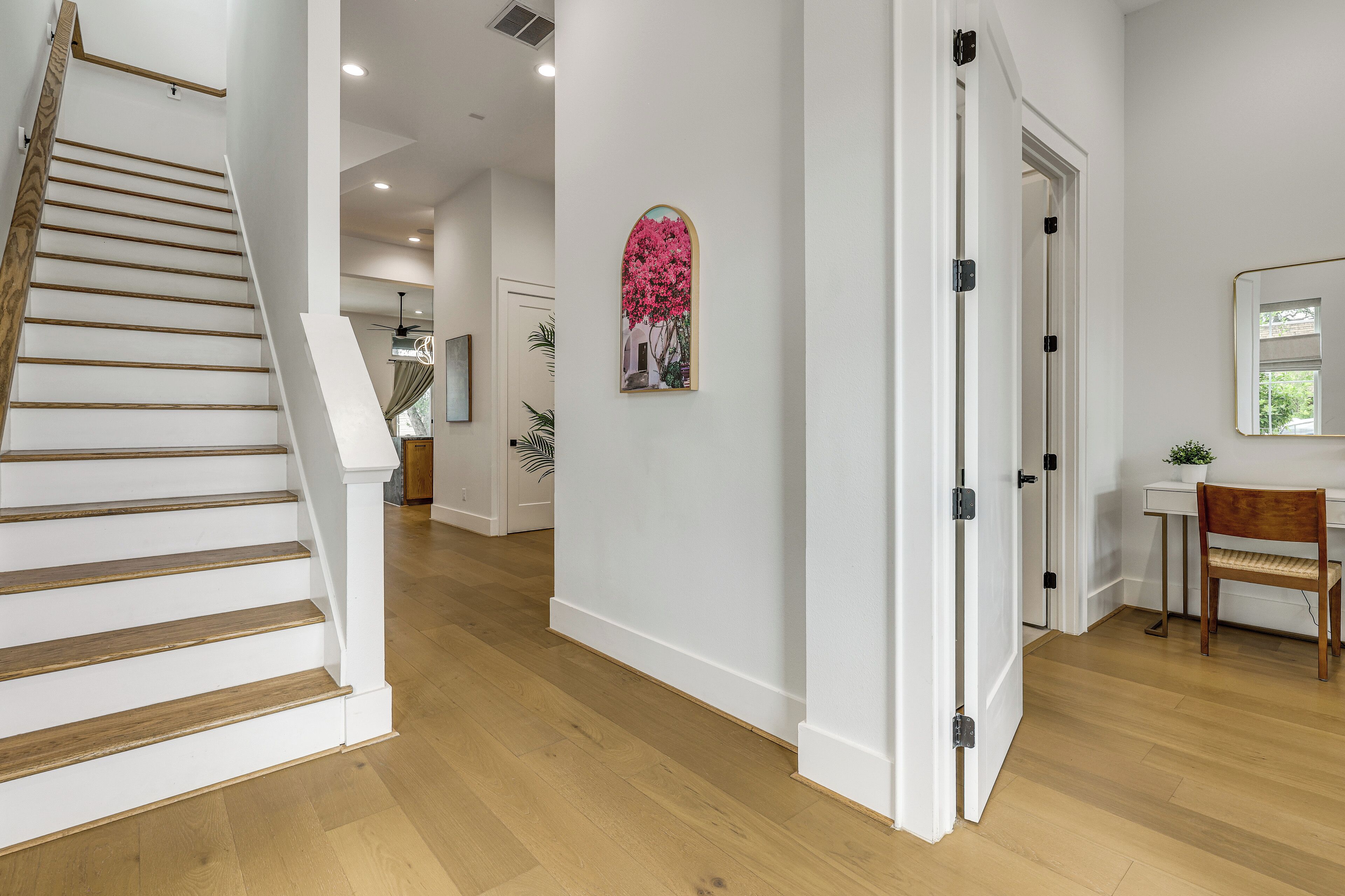 A staircase with wooden steps and white walls, leading to a room with a desk and chair.