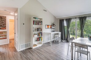 Ein Zimmer mit einer weißen Bücherwand, einem Schreibtisch und einem Essbereich mit Stühlen.