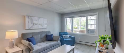 Ein Wohnzimmer mit grauem Sofa, blauem Sessel, weißem Couchtisch, einer Lampe und einem Bild an der Wand.