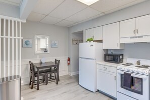 Eine Küche mit weißen Schränken, einem Kühlschrank, einer Mikrowelle, einem Backofen, einem Esstisch mit Stühlen und einem Feuerlöscher.
