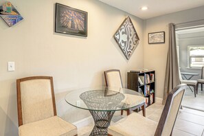 Un coin repas avec une table en verre entourée de chaises, une bibliothèque et des œuvres d’art encadrées accrochées aux murs.