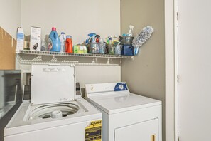 Un espace buanderie comprenant un lave-linge, un sèche-linge et une étagère où sont rangés divers produits de nettoyage.