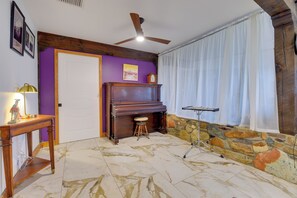 A room with a piano, a ceiling fan, a stone wall, and a door. - Experience Staying in Geodome, Pool, Hot Tub, BBQ (Tucson)