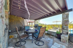 Un patio al aire libre con un muro de piedra, una zona de estar techada con una mesa y sillas, y vistas a una piscina.
