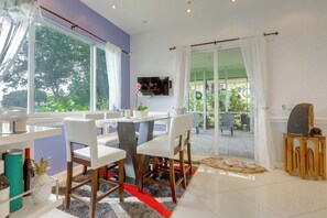 Un comedor moderno con una mesa de vidrio, sillas blancas y vistas amplias a través de grandes ventanas.