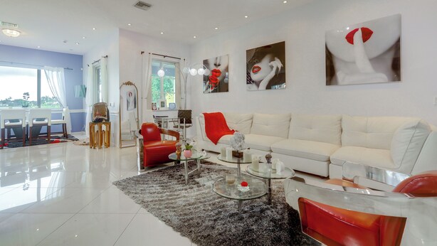 A modern living room with a white sofa, red chairs, and abstract art on the walls. - Trails & Resort Perks! Home in Royal Palm Beach (Royal Palm Beach)