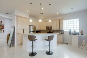 Una cocina moderna con armarios blancos, electrodomésticos de acero inoxidable e iluminación colgante.
