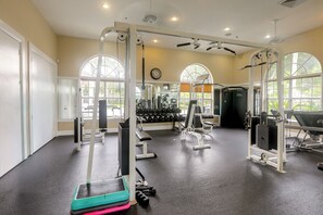 Un gimnasio con diverso equipo de ejercicio, amplias ventanas y un interior limpio y bien iluminado.
