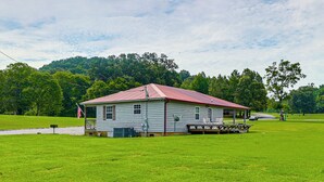 A single-story house with a red roof, a porch, and a flagpole with an American flag. - The Hunter's Retreat at Kudzu Cove Cabins Resort (Guntersville)
