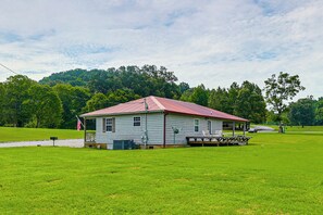 A single-story house with a red roof, a porch, and a flagpole with an American flag. - The Hunter's Retreat at Kudzu Cove Cabins Resort (Guntersville)