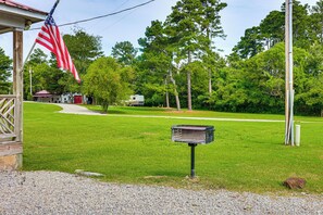 A grassy area with a mailbox, a flagpole with an American flag, and a building in the background. - The Hunter's Retreat at Kudzu Cove Cabins Resort (Guntersville)