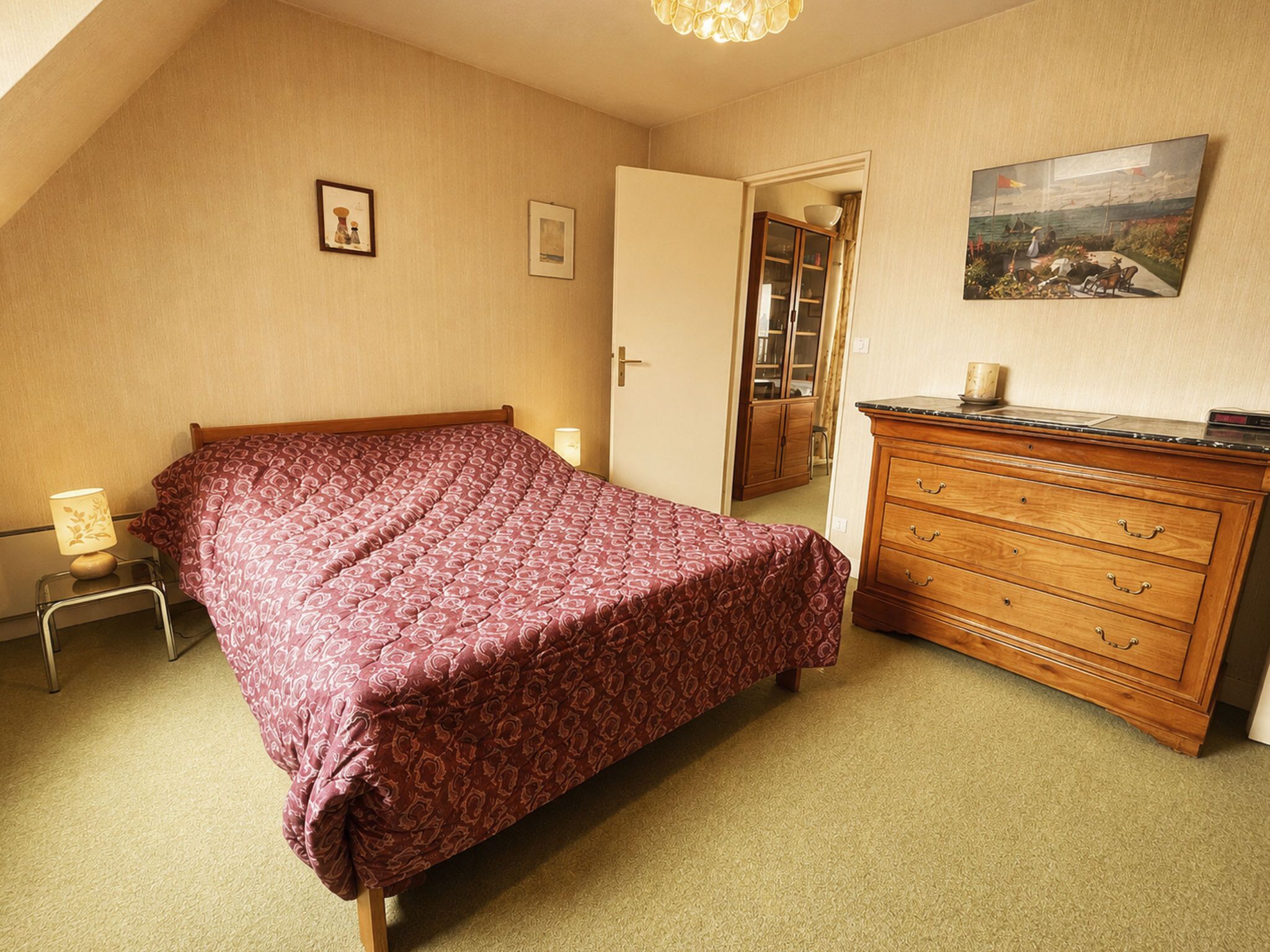 A bedroom with a bed, a dresser, a lamp, and a painting on the wall.
