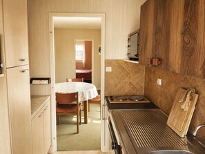 A compact kitchenette with a stove, sink, and wooden cabinets. - Les Guillemots by Interhome (Blonville sur mer)