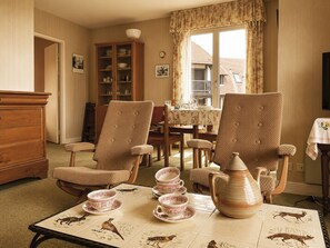 A cozy dining area with two patterned armchairs, a wooden cabinet, and a table set with plates, cups, and a teapot. - Les Guillemots by Interhome (Blonville sur mer)