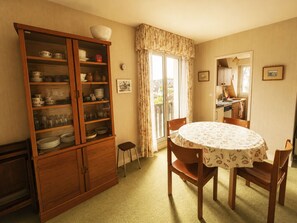 Un coin repas comprenant une table ronde, des chaises, un buffet contenant de la vaisselle et une fenêtre avec des rideaux.