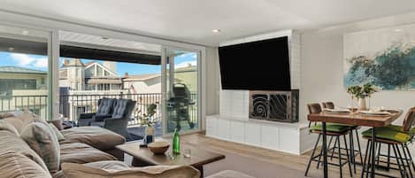 Una sala de estar moderna con un sofá grande, una mesa de comedor con sillas, una chimenea y un ventanal con vistas a una zona residencial.