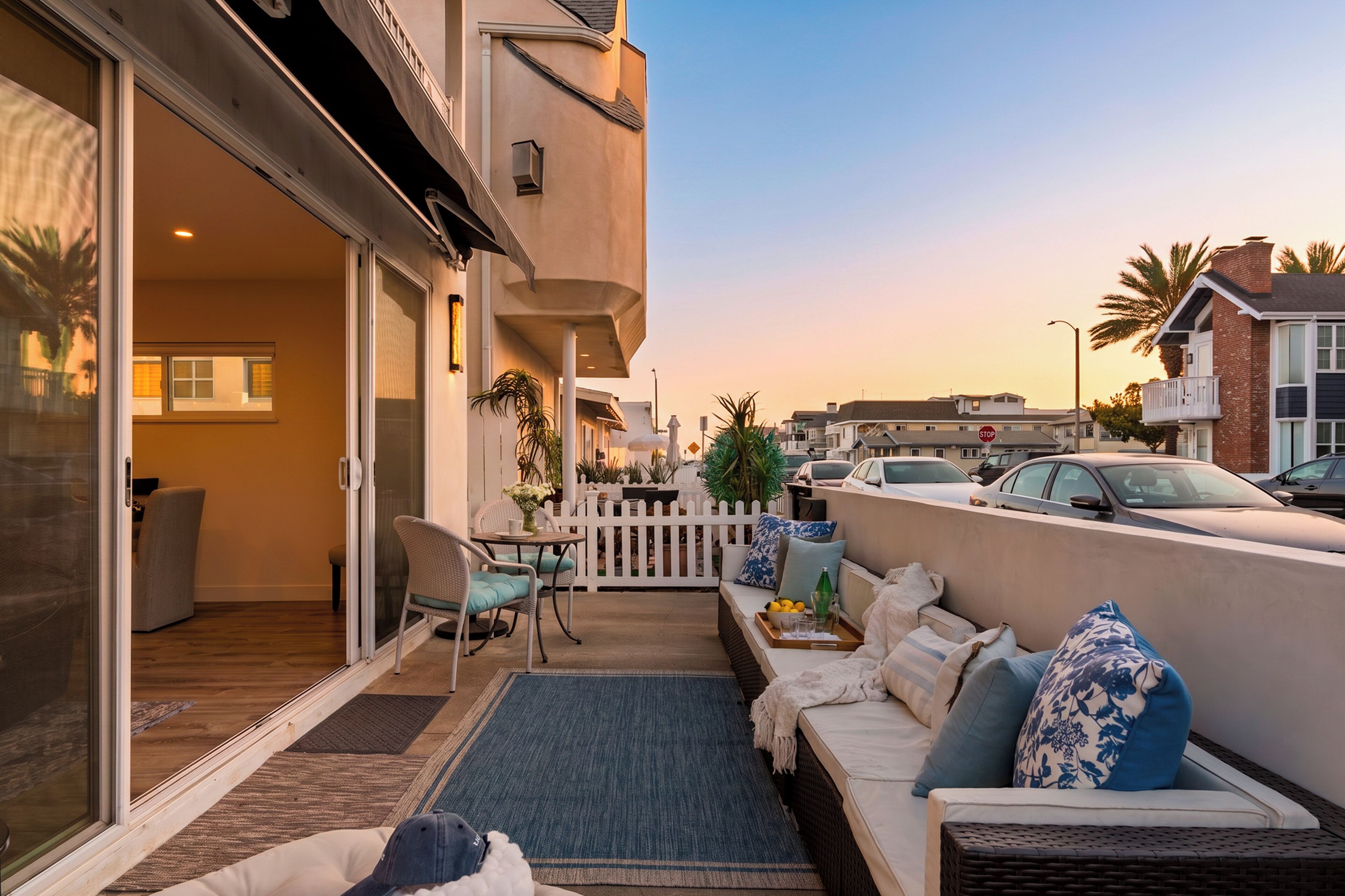 A balcony with outdoor seating, a sliding glass door, and a view of parked cars and buildings.