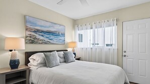 A bedroom with a bed, two bedside lamps, a painting, a window with curtains, and a door. - Entire Duplex + Steps to Beach | Newport Beach | Harborlight & Seabright Sky (Newport Beach)