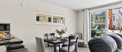 Un comedor moderno con una mesa preparada para dos personas, un banco de cuero negro y vista a un edificio residencial por una puerta de vidrio.