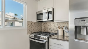A modern kitchen with a gas stove, stainless steel appliances, and a window overlooking a residential area. - Entire Duplex + Steps to Beach | Newport Beach | Harborlight & Seabright Sky (Newport Beach)