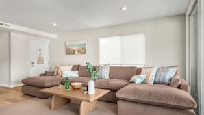 A living room with a brown sectional sofa, a wooden coffee table, and a window with blinds. - Entire Duplex + Steps to Beach | Newport Beach | Harborlight & Seabright Sky (Newport Beach)