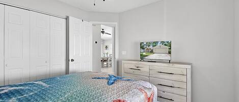 A bedroom with a bed, a dresser, a ceiling fan, and a television.