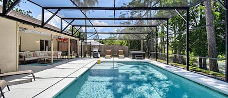 A covered outdoor swimming pool with a patio area, seating, and a barbecue grill.
