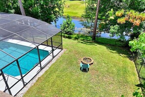A swimming pool with a glass enclosure, a fire pit, and a grassy area with trees. - Shady Pines Sea-renity | Waterfront Pool & Hot Tub | Golf Nearby | Palm Coast | Close To Beach (Palm Coast)