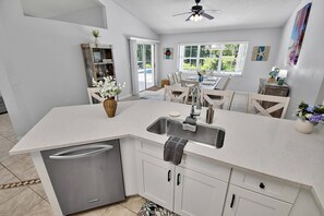 A modern kitchen with a central island, stainless steel appliances, and a dining area with natural light. - Shady Pines Sea-renity | Waterfront Pool & Hot Tub | Golf Nearby | Palm Coast | Close To Beach (Palm Coast)