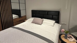 Ein modernes Schlafzimmer mit einem großen Bett, einem Nachttisch mit einer Vase und einem Spiegel.