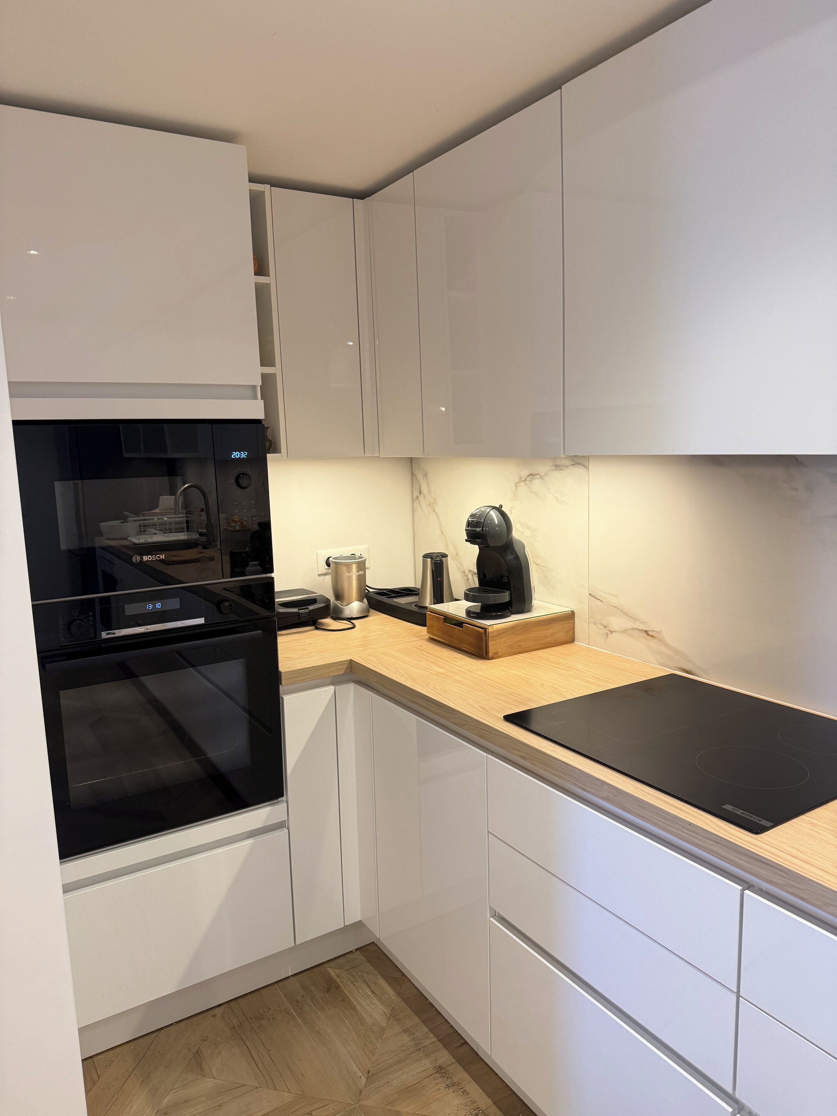 A modern kitchen with white cabinetry, a Bosch oven, a coffee maker, and a black induction cooktop.