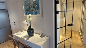 Eine moderne Küche mit weißer Arbeitsplatte, einem Holzhocker, einer Blumenvase und einem gerahmten Kunstwerk an der Wand.