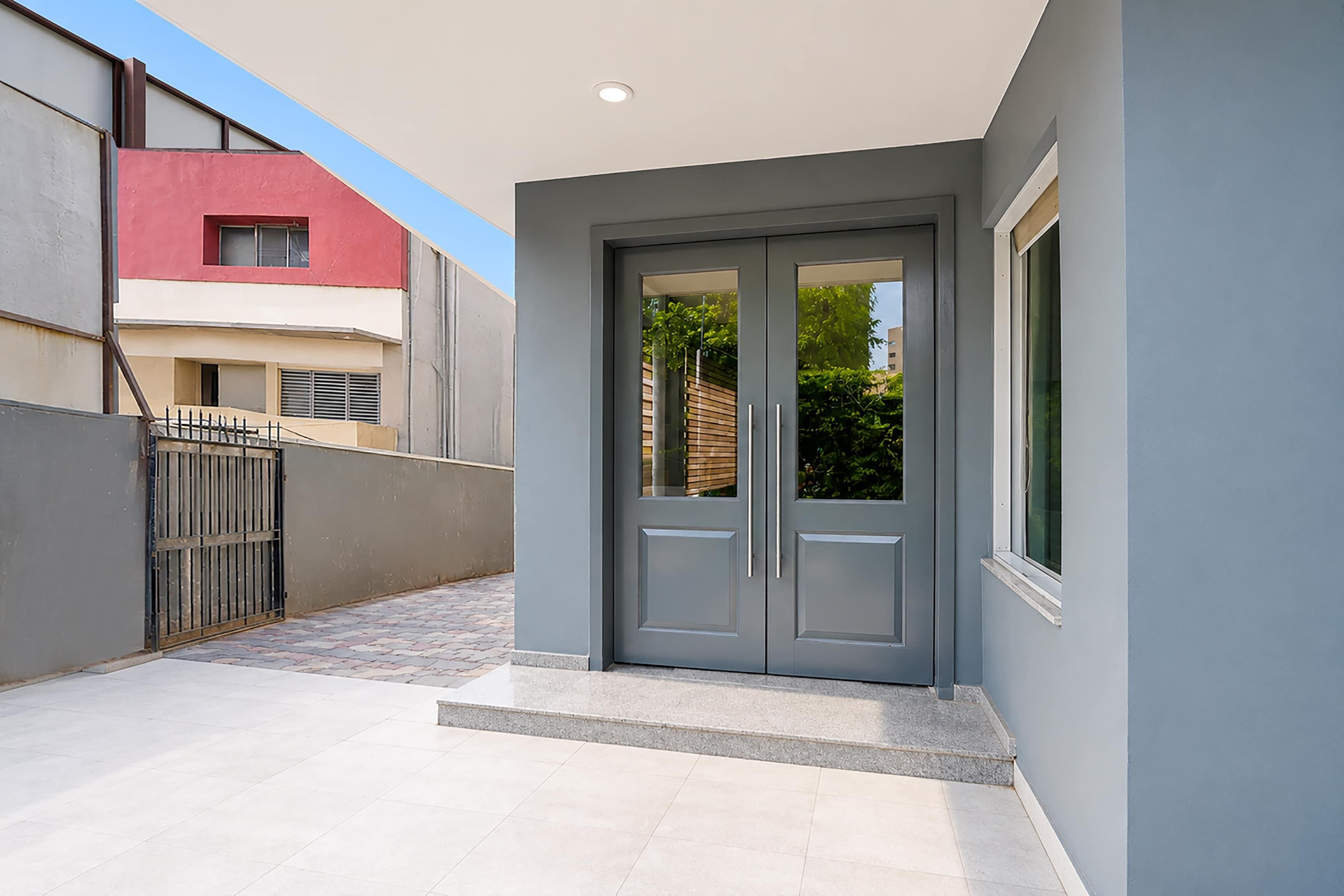 Un edificio moderno con fachada gris, entrada protegida por una reja y un patio con pavimento de baldosas.