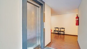 Un pasillo con una puerta cerrada, un extintor y dos sillas.