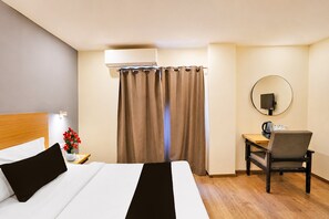 Habitació d'hotel amb un llit, una taula de treball amb una cadira, un mirall rodó i una finestra amb cortines.