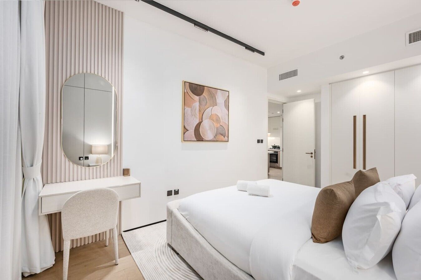 A modern hotel room with a bed, a desk, a chair, a large mirror, and a painting on the wall.