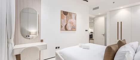 A modern hotel room with a bed, a desk, a chair, a large mirror, and a painting on the wall.