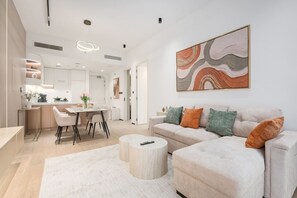 A modern living room with a sofa, coffee table, and a dining area with chairs. - FIRST CLASS | 1BR | Modern Haven | Tranquil City (JVC)