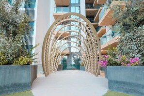 A modern building with a central walkway flanked by planters with greenery and flowers. - FIRST CLASS | 1BR | Modern Haven | Tranquil City (JVC)