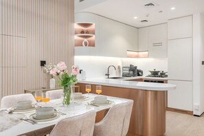 A modern kitchen with a central island, a dining area with a table set for four, and a decorative vase with flowers. - FIRST CLASS | 1BR | Modern Haven | Tranquil City (JVC)