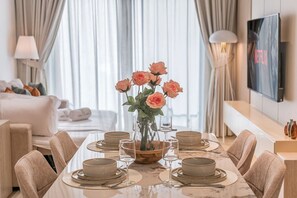 A dining area with a table set for four, a vase with flowers, and a television on the wall. - FIRST CLASS | 1BR | Modern Haven | Tranquil City (JVC)