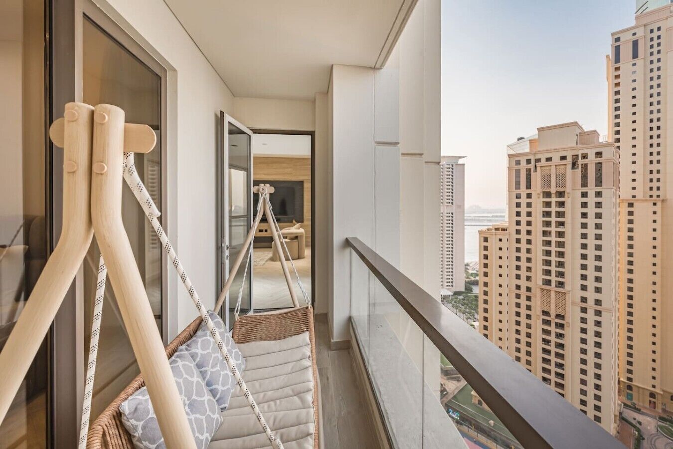 A balcony with a hanging chair, a view of tall buildings, and a glimpse of the interior.