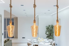 A modern dining area with a table set for four, hanging pendant lights, and a plant in the background. - FIRST CLASS |2BR| Marina Views | Near JBR Beach (JBR)