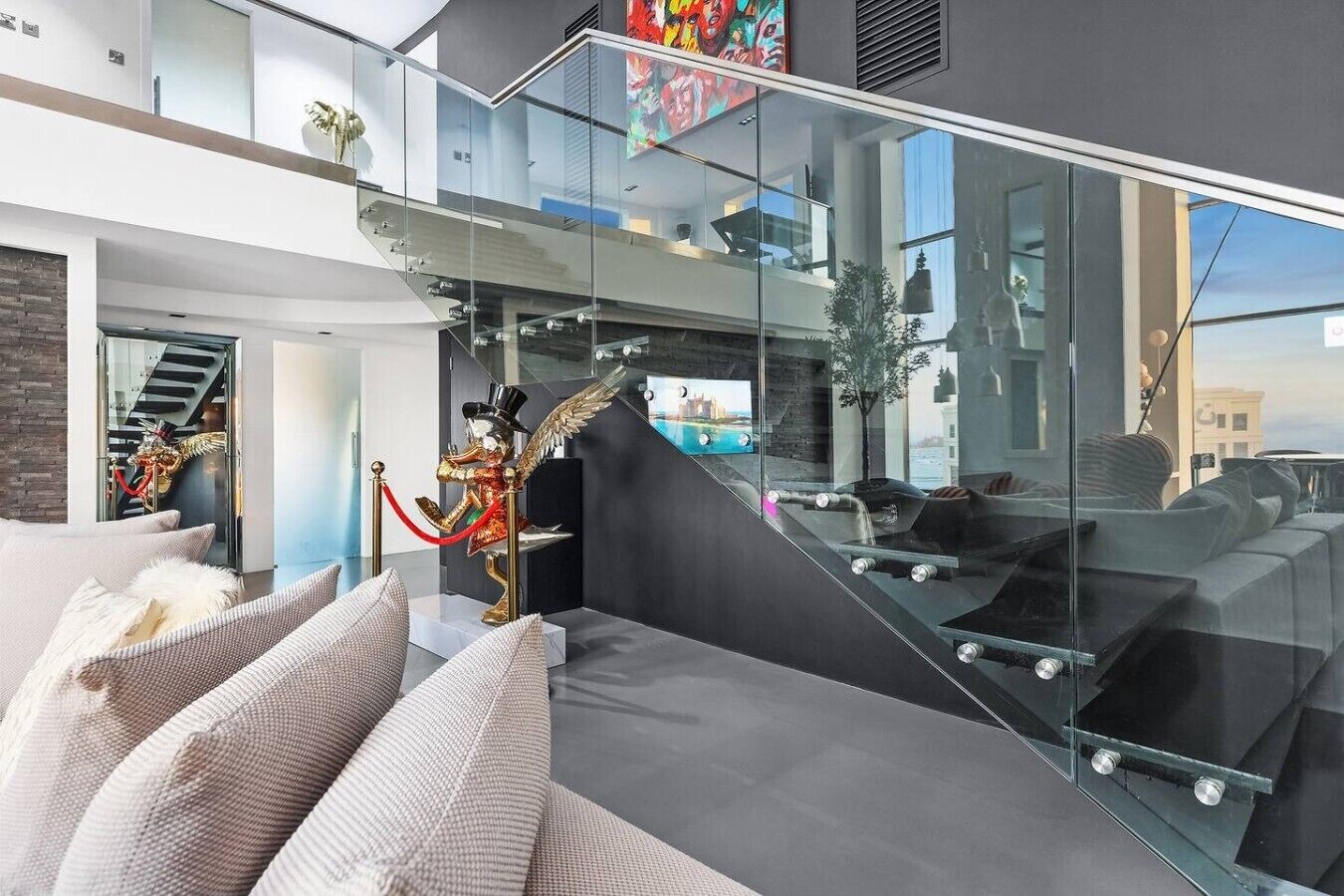 A modern interior with a glass staircase, a statue, and a view of the city.