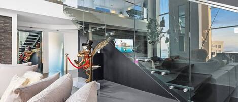 A modern interior with a glass staircase, a statue, and a view of the city.