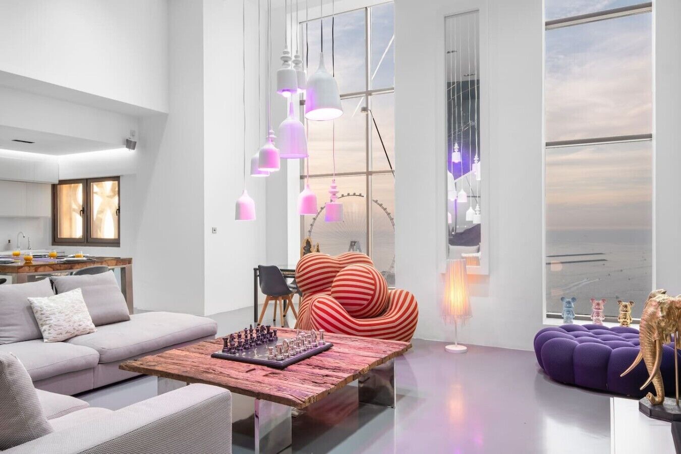 Una sala moderna con un sofá, una mesa de centro con piezas de ajedrez, un sillón a rayas y un sofá púrpura.