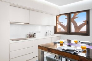 A modern kitchen with white cabinets, a wooden dining table with two chairs, and a window with a tree view. - FIRST CLASS |3BR| Luxury Duplex w/ Ain Dubai View (JBR)